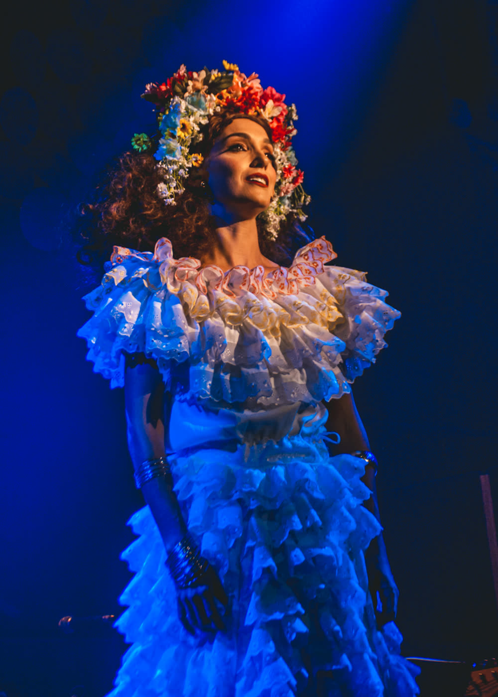 Bruna Pazinato em cena, coroa de flores e luz azul